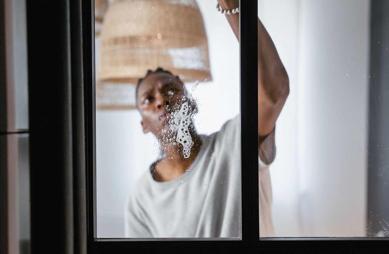 An adult male cleaning a glass window indoors, emphasizing household chores and a clean environment.